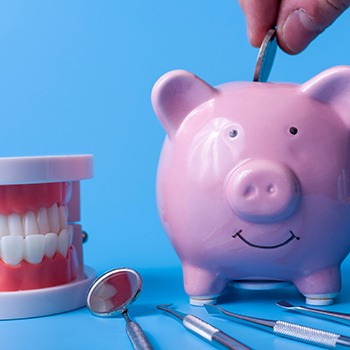 A piggy bank on a blue background next to various dental instruments