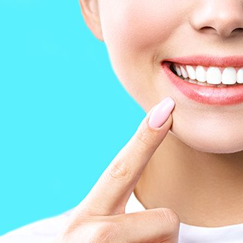 Nose-to-neck view of woman pointing to her bright smile with pointer with light blue background